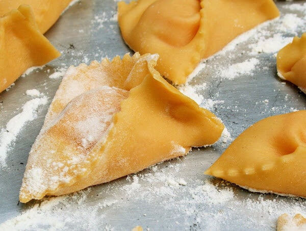 A sheet pan filled with uncooked pumpkin ravioli.