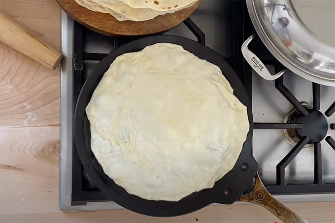 A flour tortilla cooking in a skillet. 