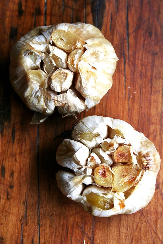 Roasting garlic whole tames its bite, mellows and sweetens its flavor, and transforms it into a butter-like purée almost as tasty as salted bone barrow. These whole roasted garlic heads go perfectly with bread. // alexandracooks.com An overhead shot of two heads of roasted garlic.