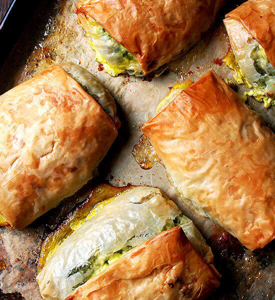 Five baked spanakopita strudels on a sheet pan.