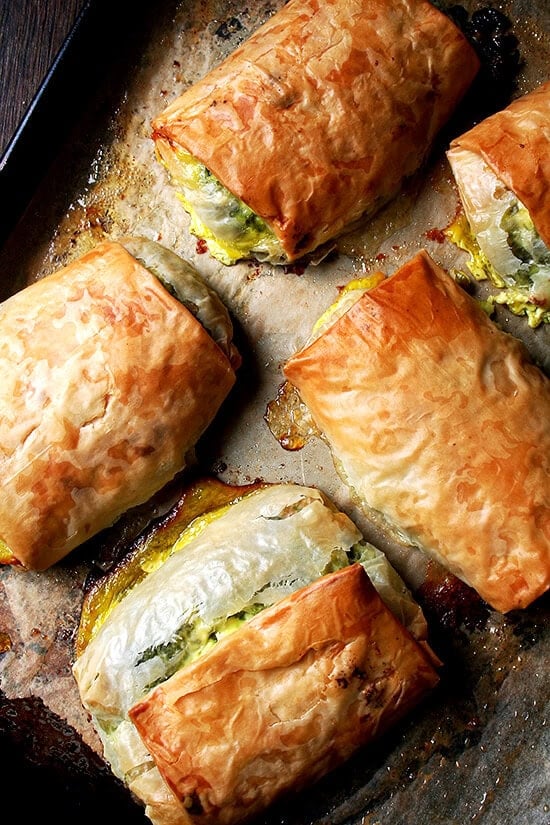 Five baked spanakopita strudels on a sheet pan. 