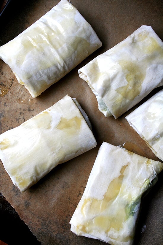 Unbaked spanakopita strudels on a sheet pan. 