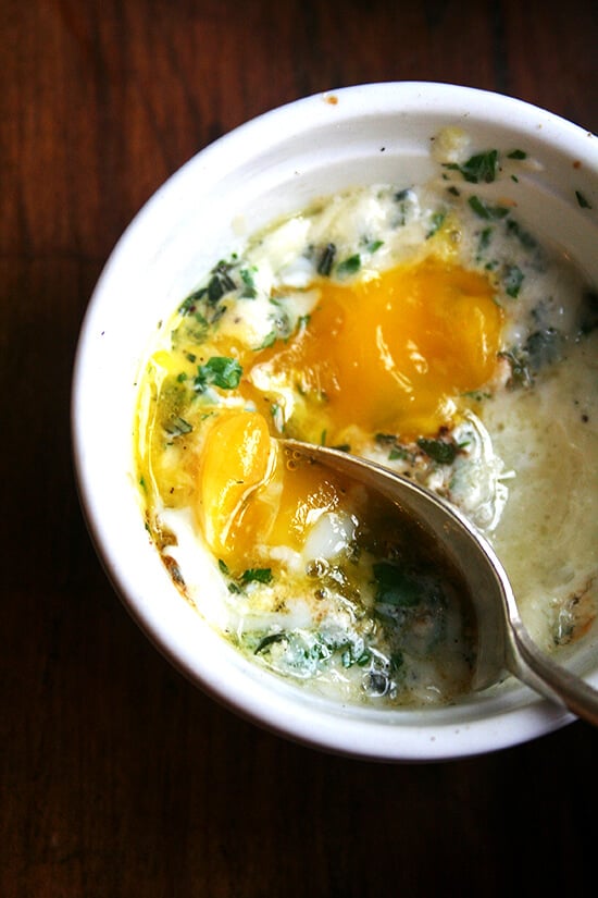 This recipe for baked eggs appeared in the New York Times Magazine in 1985, and my mother has been making them for us ever since. Topped with herbs — parsley, sage, rosemary and thyme — melted gruyère and a few splashes of Tabasco, these perfectly soft-cooked eggs are such a treat. // alexandracooks.com A ramekin holding a baked (shirred egg) with a spoon.