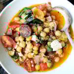 A bowl of stewy chickpeas with tomatoes and basil.