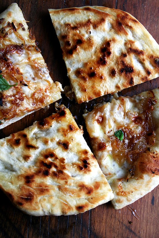 The under carriage of a caramelized onion and burrata pizza sprinkled with basil.