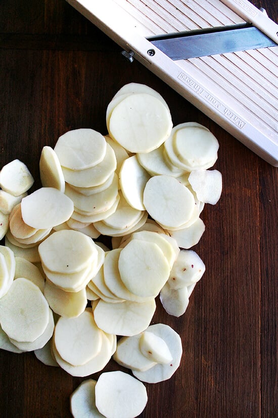 A mandoline with sliced potatoes on a board. 