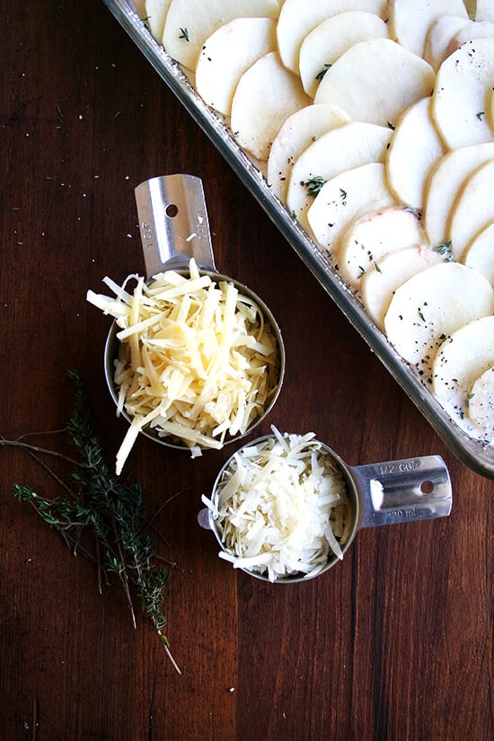 Grated parmesan and Gruyère in measuring cups aside potato gratin.