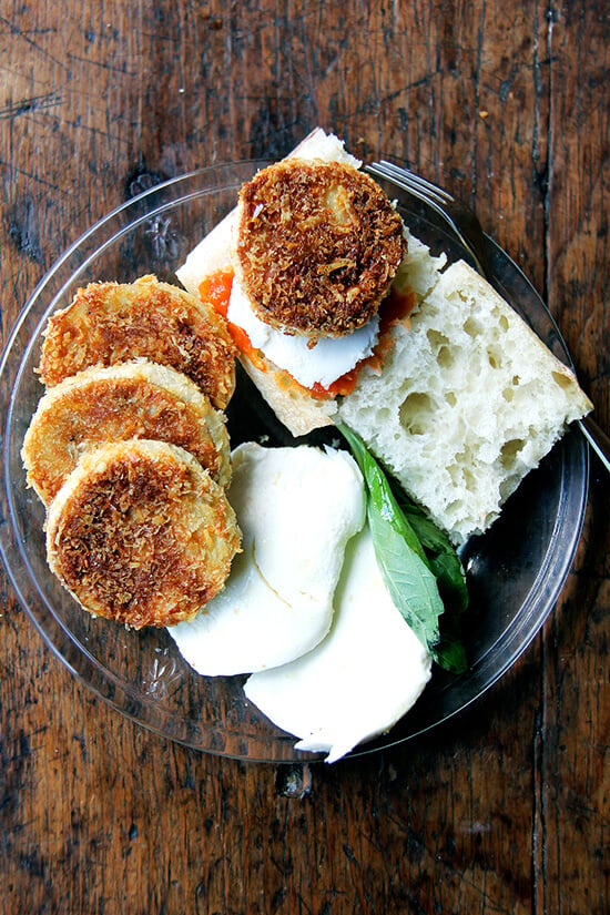 A plate of crispy eggplant rounds, tomato, mozzarella, bread, and basil.