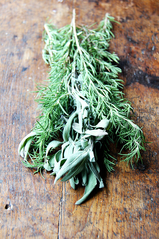 A few sprigs rosemary and sage on a board.