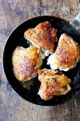 A skillet filled with crispy chicken thighs and preserved lemon.