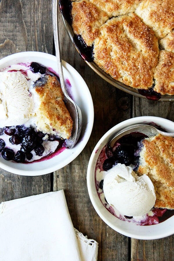 The idea behind this blueberry cobbler is that the blast of heat from the bubbling berries helps cook the underside of the biscuits, while the hotter temperature of the oven nicely browns the top. The result? An evenly cooked — not dry! — tender, golden biscuit. // alexandracooks.com Bowls of blueberry cobbler with ice cream.