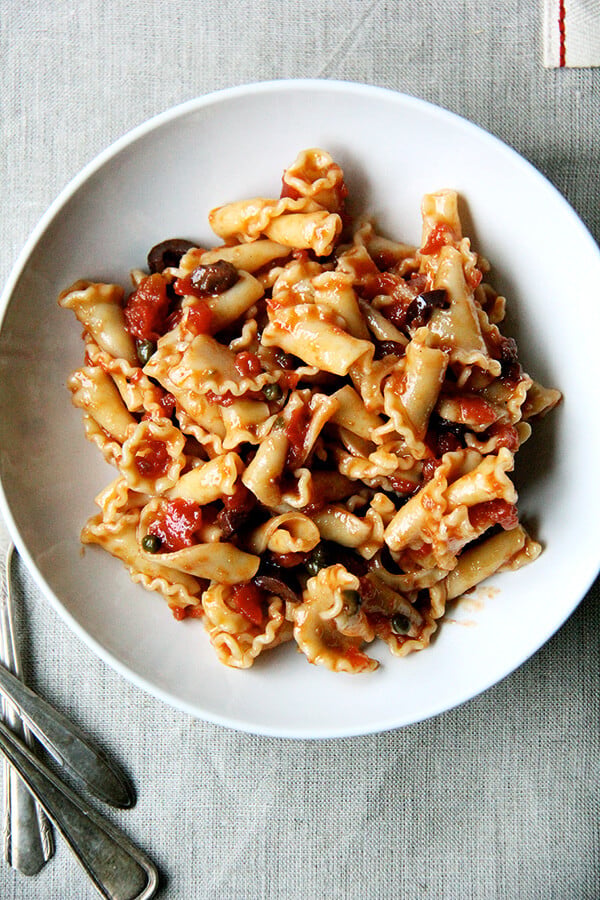 The hardest part about making this puttanesca is smashing a few cloves of garlic and coarsely chopping a half cup of olives. The rest comes from pantry staples: plum tomatoes, anchovies, capers. After an hour of simmering, the plum tomatoes break down, the anchovies dissolve, the cloves of garlic melt. The sauce can certainly be made ahead and the pasta cooked just before dinner, which makes for easy preparations at the dinner hour. // alexandracooks.com A plate of pasta tossed with puttanesca sauce.