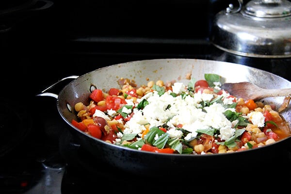 A sauté pan with chickpeas, olive oil, garlic, basil, capers, and feta.