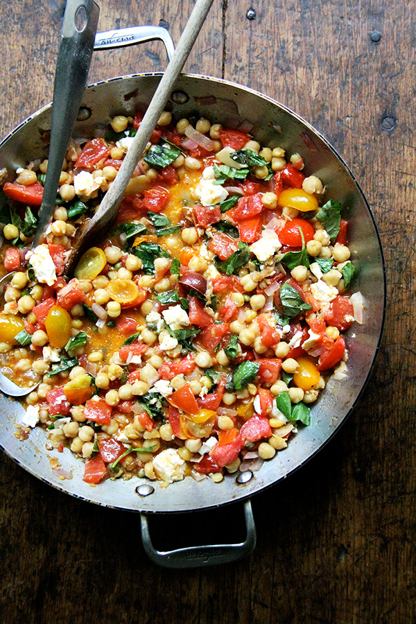 These stewy chickpeas are a mix of chickpeas, tomatoes, basil, and feta. After I made it the first time, we devoured most if it immediately with crusty, olive oil-toasted bread, then snacked on the leftovers for days. // alexandracooks.com A sauté pan with stewy chickpeas, tomatoes, garlic, and basil.