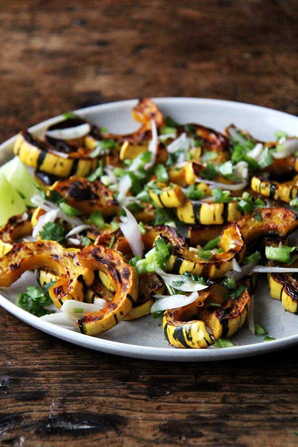 Roasted delicata squash, if you are unfamiliar, is one of the easiest of all the squashes to prepare. You can cut through its skin easily with a knife, and you can eat the skin once roasted—it's truly delicious. Here, a tart dressing, made with shallots and jalapeños macerated in lime juice, so nicely complements the sweet squash, and a showering of cilantro at the end offers a blast of freshness. // alexandracooks.com Roasted delicata squash on a platter topped with chilies, lime, and cilantro.