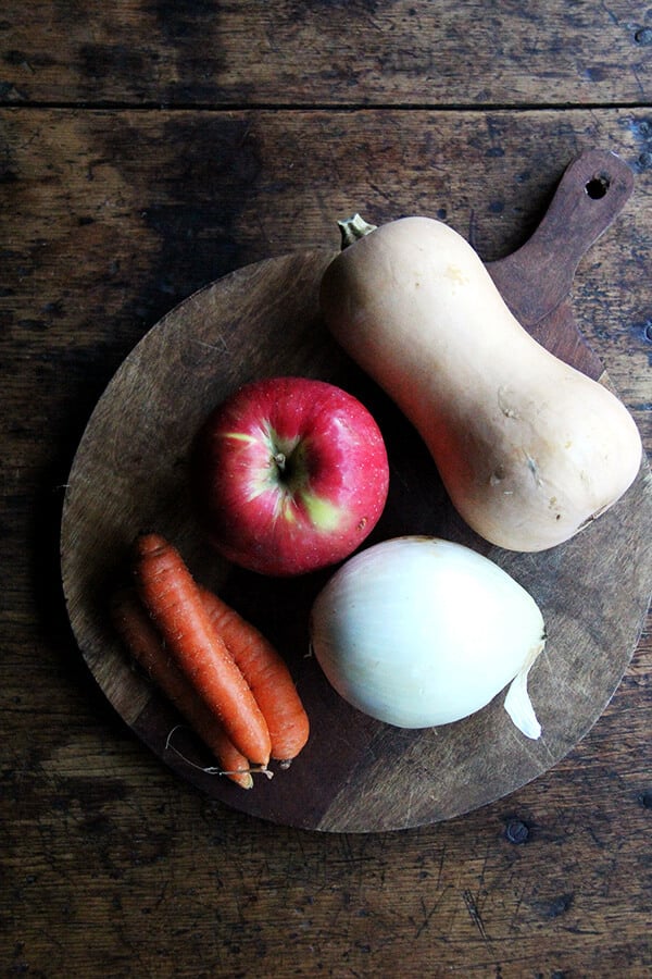 A board of ingredients: apple, onion, carrots, and butternut squash.