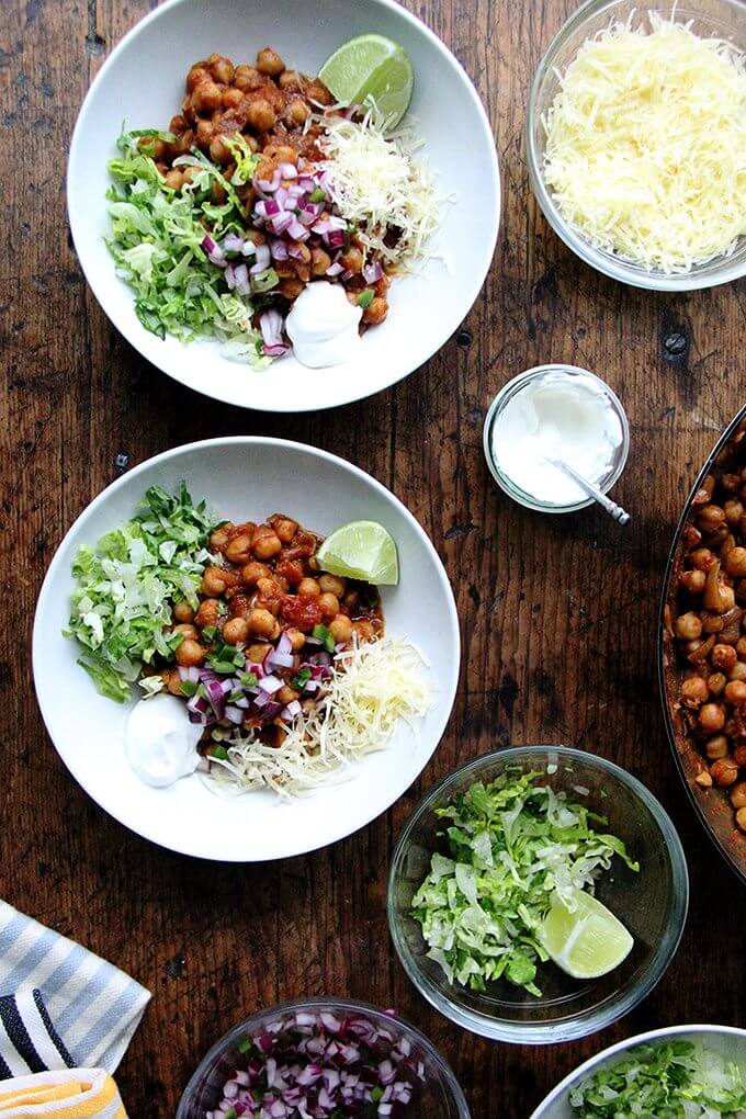 In these chickpea taco bowls, the chickpeas swell with the smoky, spicy, earthy flavors of the chili powder, cumin, crushed tomatoes, and garlic. Sweat the onions, add the seasonings, liquid, and protein, and simmer till flavorful. Yum. // alexandracooks.com Assembled chickpea taco bowls with lettuce, lime, sour cream, and cheese.