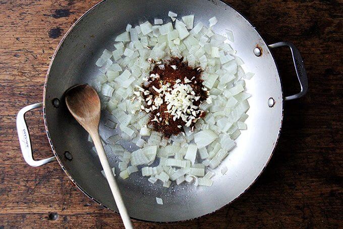 A sauté pan with onions, spices, and garlic.