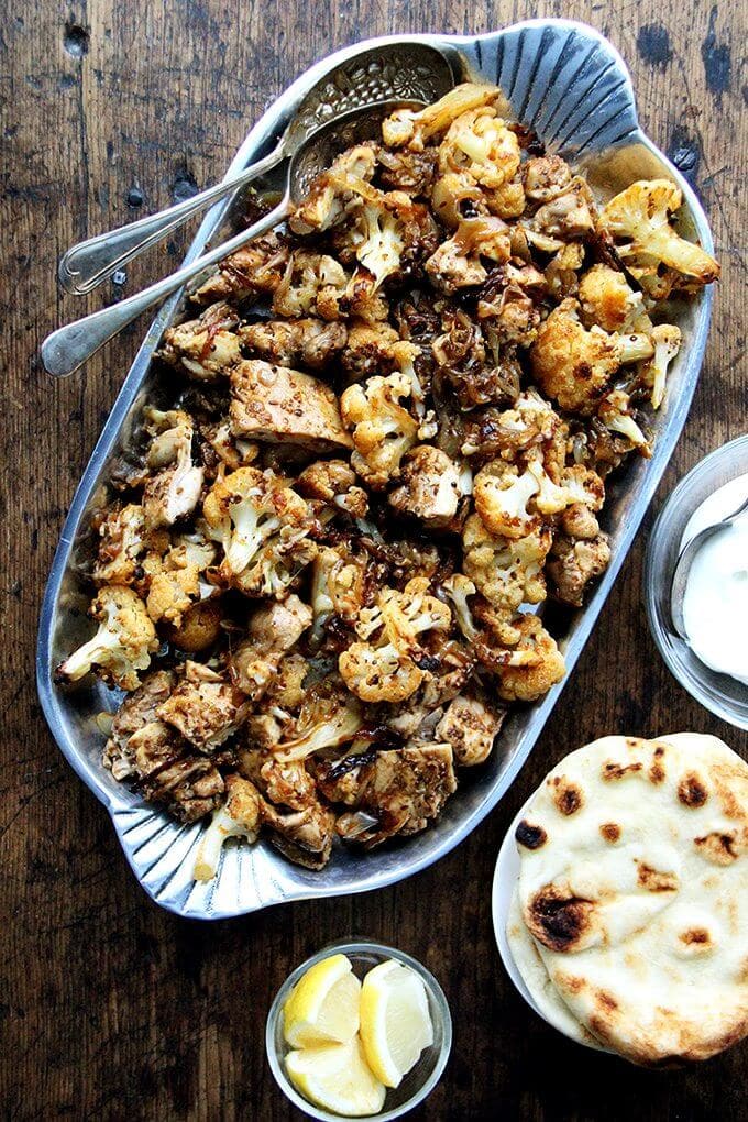 Heres the gist of this sheet pan chicken and cauliflower "shawarma": cauliflower florets, a sliced onion, and a few unpeeled garlic cloves dressed with olive oil and a few thyme sprigs roast for 40 minutes on a sheet pan, where they caramelize before they meet a showering of salty, grated parmesan. The combination of sweet and salty, as you can imagine, is incredibly delicious. // alexandracooks.com A platter of sheet pan chicken and cauliflower shawarma.