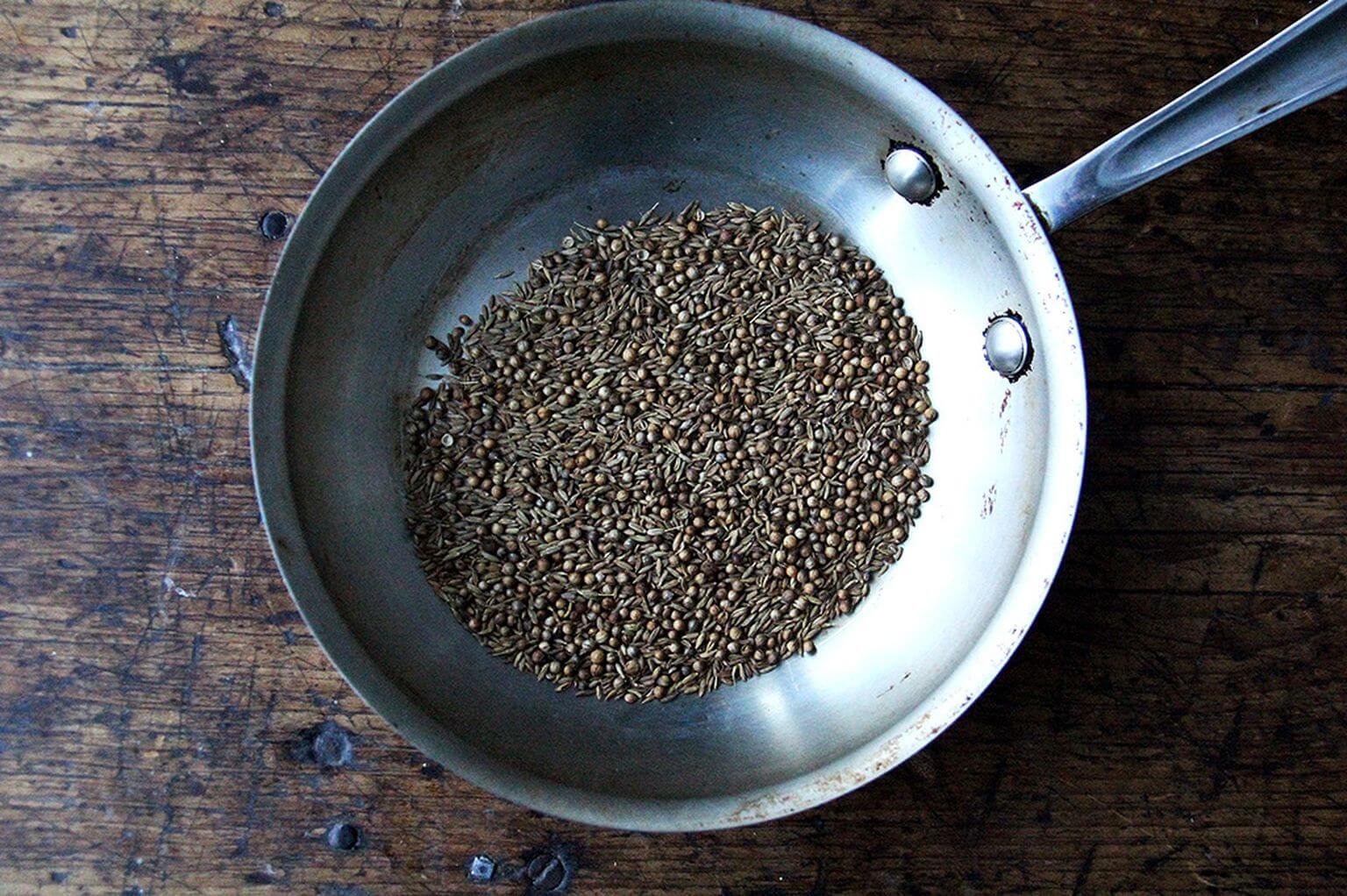 A skillet of cumin and coriander seeds.