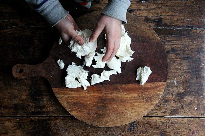 A child tears mozzarella over a board.