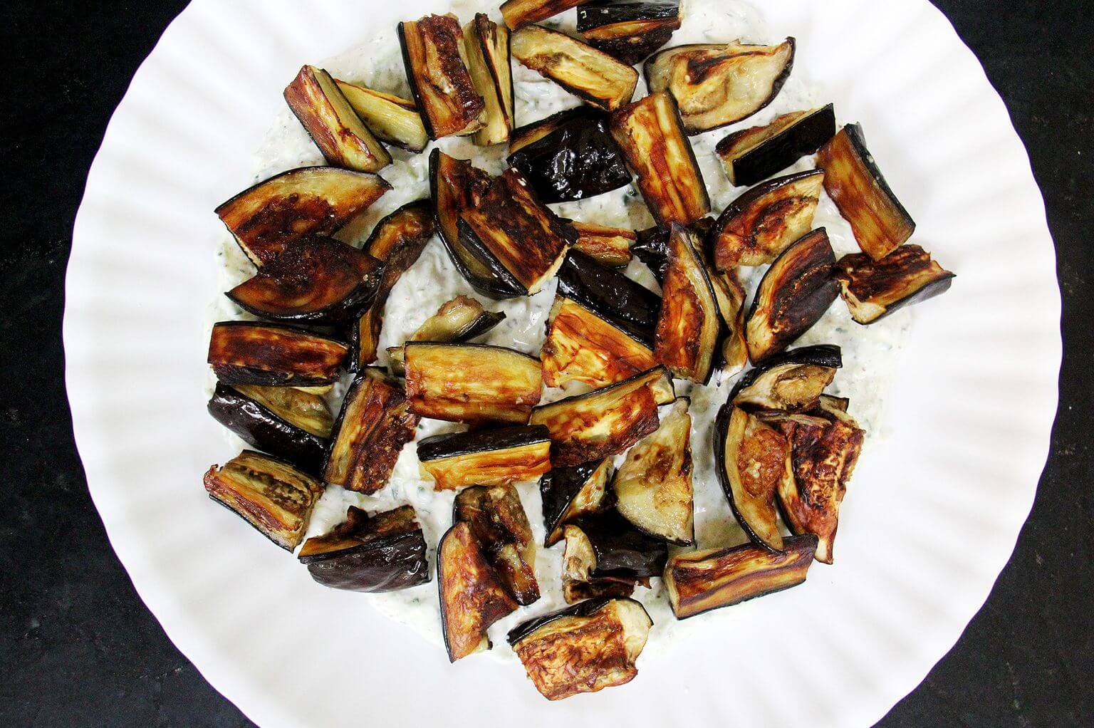 A platter with tzatziki smear and roasted eggplant.