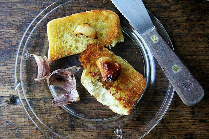 A plate topped with bread and whole cloves of roasted garlic.