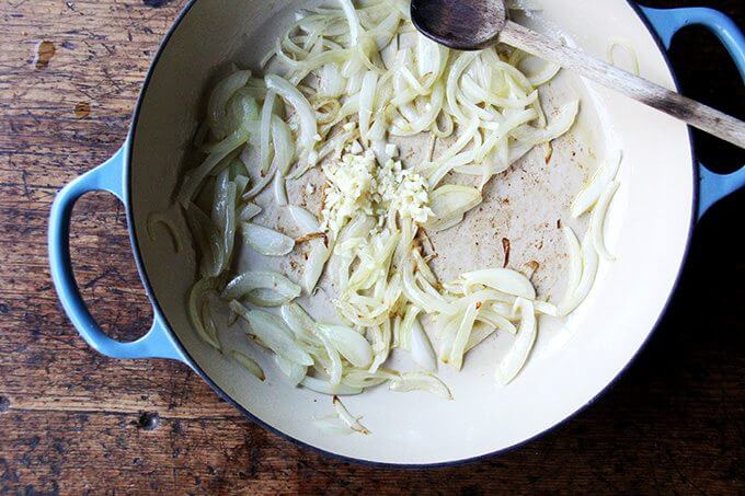 A Le Creuset braiser filled with onions and garlic.