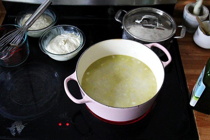 An overhead shot of a stovetop holding a large pot of cabbage soup and two bowls of rising bread dough.