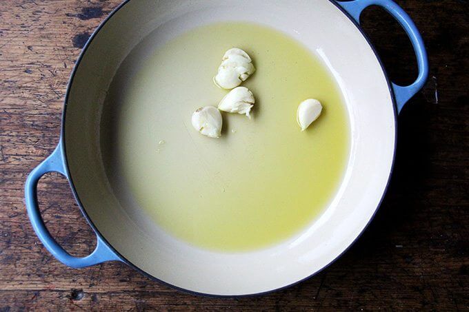 A braiser filled with oil and whole garlic cloves.