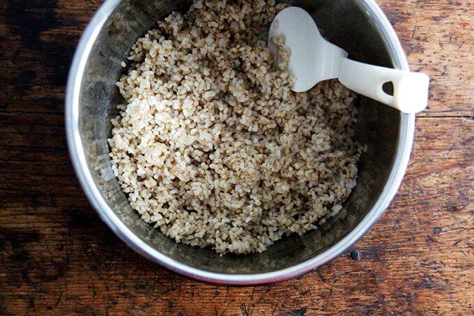 An uncovered Instant pot filled with perfectly cooked Instant Pot brown rice and a plastic spoon.