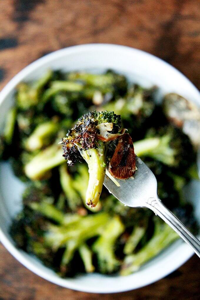 This roasted broccoli recipe is excellent and easy. I've made it three times in my portable Waring oven on two mini sheet pans in the past week because it just tastes so darn good right now—it's just what I'm craving after many weeks of indulging. // alexandracooks.com A bite of roasted broccoli with garlic on a fork.