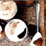 Chocolate pots de creme covered with chocolate shavings on a board.