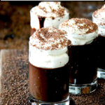 Chocolate pots de creme in small glasses topped with whipped cream on a board.