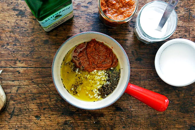 A sauce pan with olive oil, harissa, garlic, and cumin.