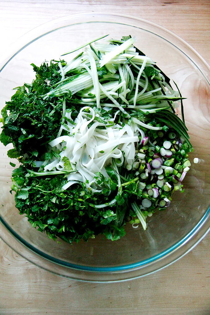 Cooked rice noodles with herbs and cucumbers in a bowl.