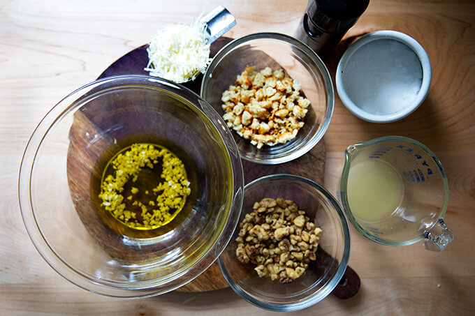 The ingredients for a walnut salsa: olive oil, minced garlic, parmesan, bread crumbs, walnuts, lemon, salt, and pepper.