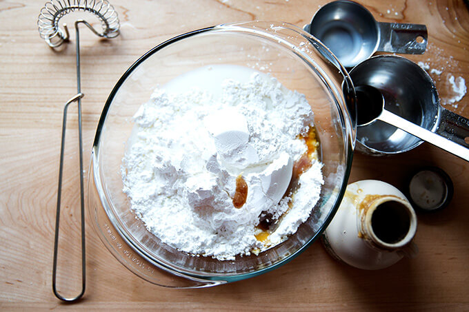 The ingredients for the maple glaze in a bowl aside measuring cups, spoons, and a whisk.