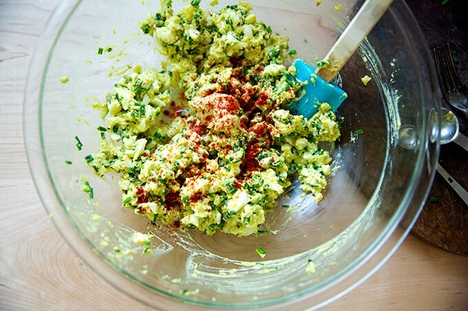 Adding the paprika and mustard to the bowl of hard-boiled eggs and avocado.