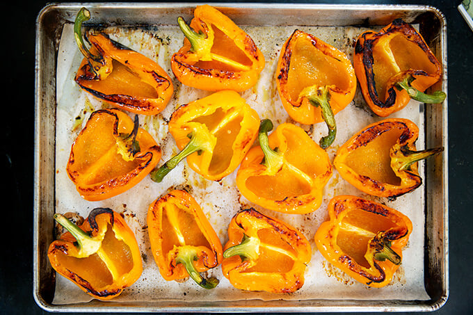 A sheet pan with blistered orange bell peppers cut side up.