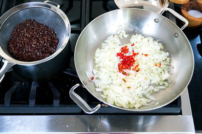 A sauté pan with onions and chili aside a pot of cooked quinoa.