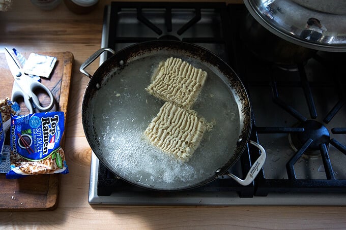 A sauté pan on the stovetop filled with boiling water and ramen noodles.