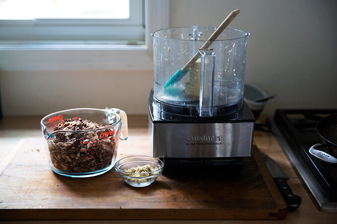 An empty food processor aside a liquid measure filled with chopped mushrooms and chopped ginger.