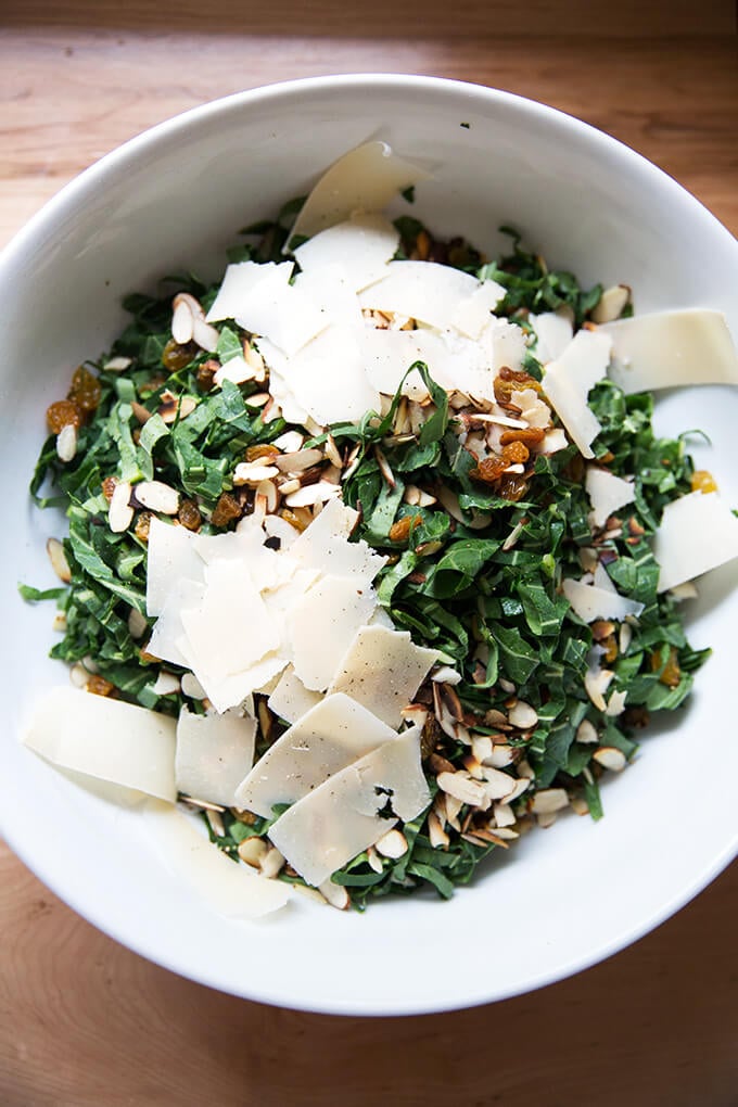 A bowl of shaved collard greens, almonds, golden raisins, and shaved parmesan.