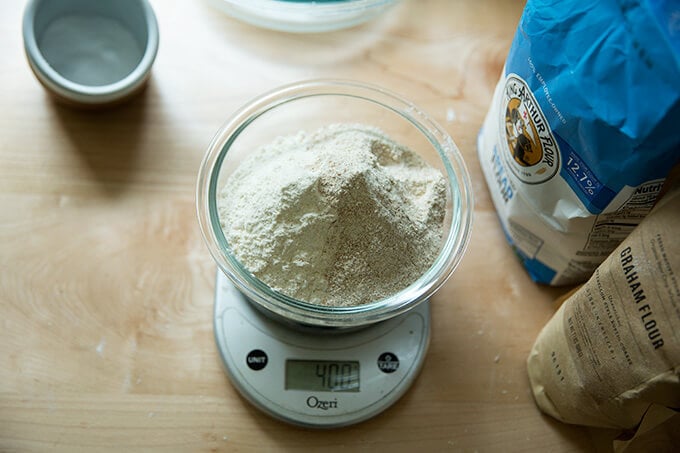 A bowl on a scale filled with bread flour, graham flour, and rye flour.