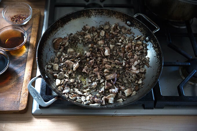 A large sauté pan filled with chopped mushrooms being sautéed in olive oil.