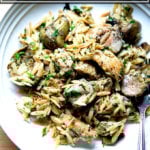 An overhead shot of a white plate with lemon, orzo, chicken and artichoke hearts.