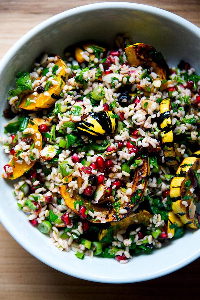A white serving bowl filled with winter tabbouleh and roasted delicata squash slices.
