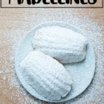 Lemon madeleines dusted in powdered sugar on a cooling rack.