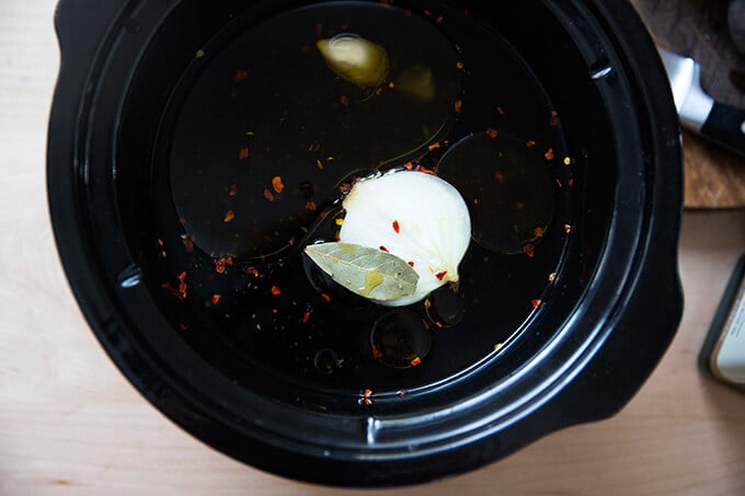 Overhead shot of a crock pot filled with black beans, water, oil, and aromatics, ready to simmer.